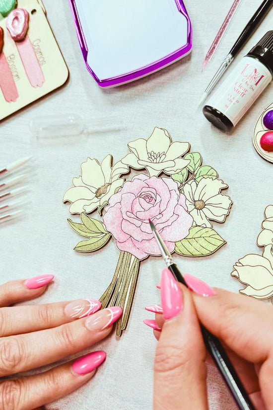 Hands painting wooden floral design from adult craft kit using shimmer watercolour paints