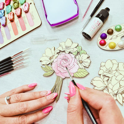 Hands painting wooden floral design from adult craft kit using shimmer watercolour paints